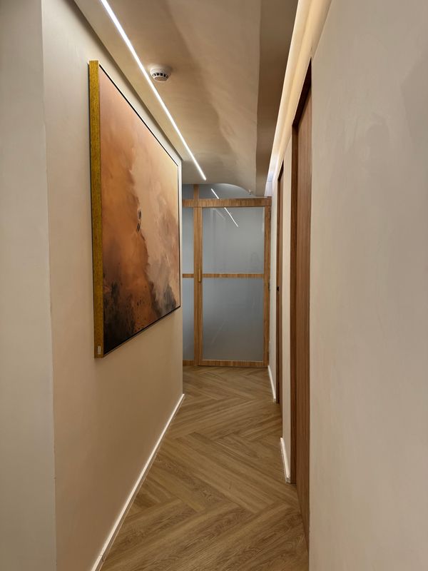 Corredor de circulação do consultório, com piso de madeira e quadro decorativo