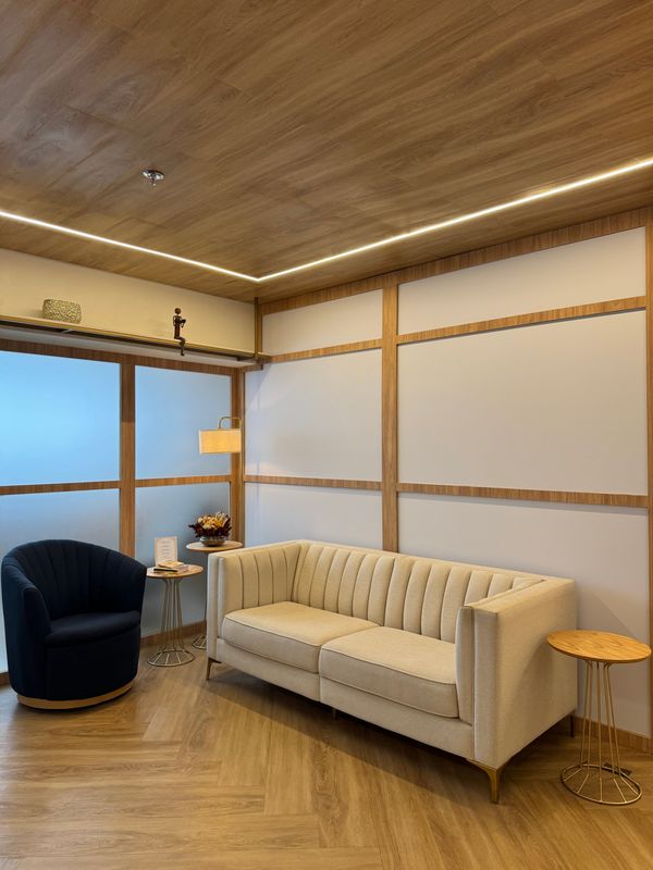Sala de espera com sofá, poltrona azul-marinho e iluminação suave