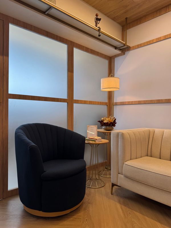 Detalhe da sala de espera, com poltrona azul-marinho, sofá e luminária
